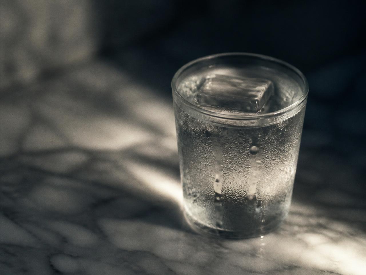 Chilled glass of iced water with condensation on a cool grey marble surface.
